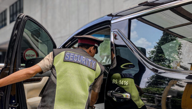 Seorang petugas CityGuard yang mengenakan rompi reflektif sedang memeriksa sebuah kendaraan di fasilitas publik. Ia membuka pintu mobil dengan cermat, menunjukkan ketelitian dan profesionalisme CityGuard dalam jasa security fasilitas publik.